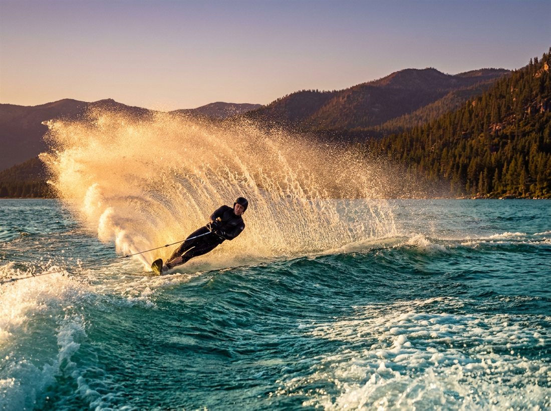 A slalom water-skier carving a hard turn, throwing a wall of golden spray.